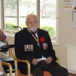 A resident with army medals sits and listens to Anzac Day presentations with palm cards in his hands