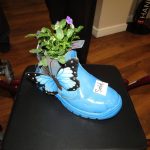 A blue boot with a plant growing inside it with the label 'Sold'