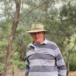 A man in a slouch hat smiles in the Australian bush