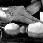 A man carves wood into intricate shapes in a close up of his hands and the tools