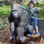 A child posing with a gorilla statue in a garden